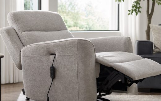 Electric reclining armchair in a modern living room with a partially extended footrest, side-mounted wired controller, upholstered seat, and visible reclining mechanism
